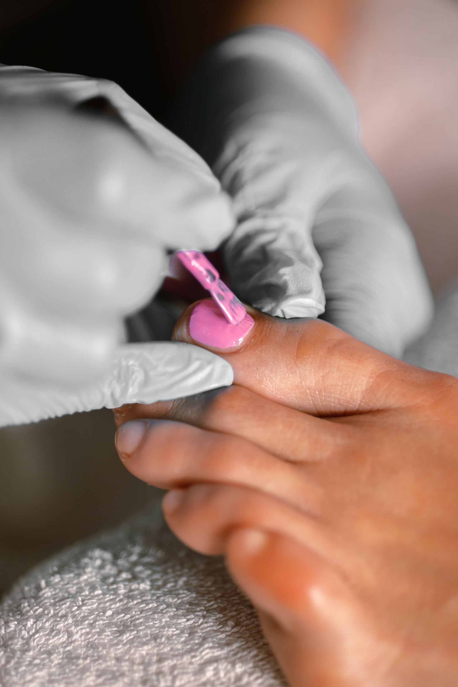 Detailed view of a pedicure session with pink nail polish applied by a beautician wearing gloves.
